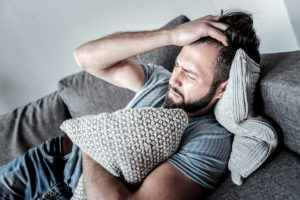 man in pain on couch showing telltale addictive behaviors