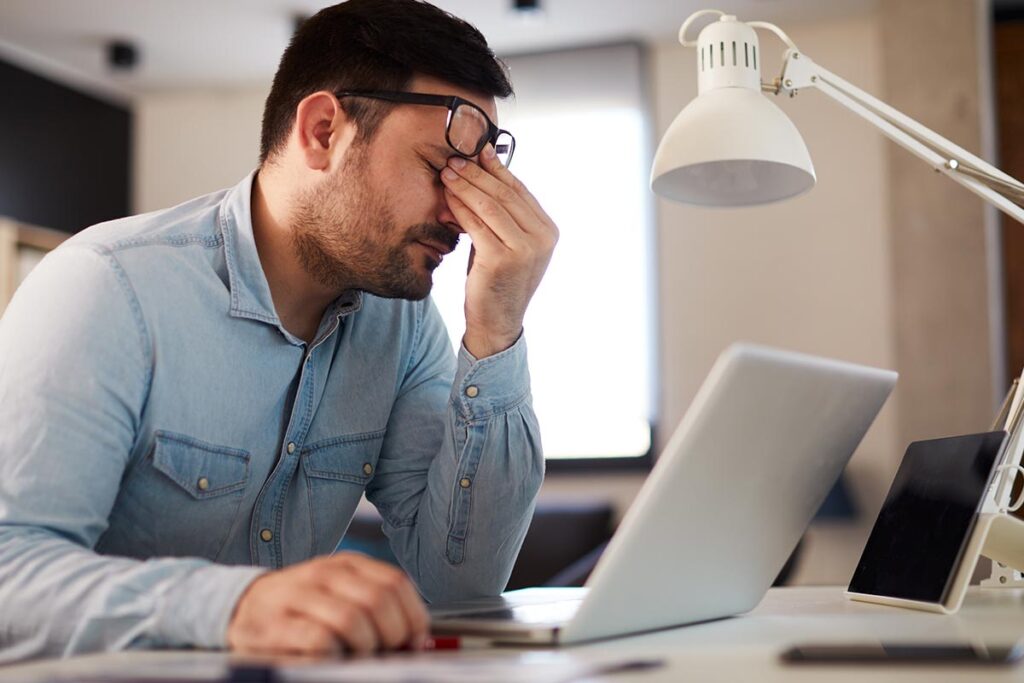 a man covers his face as he considers negative health effects of compulsive work addiction