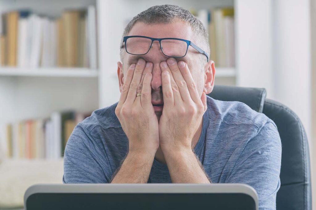 a man covers his eyes as he considers the dangers of being sleep deprived