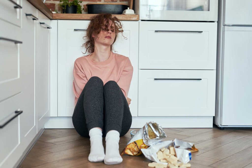 Person sitting on kitchen floor struggling with health effects of bulimia