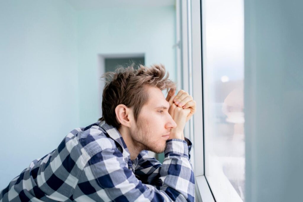 Man looking out of window thinking about the connection between mental disorders and drinking