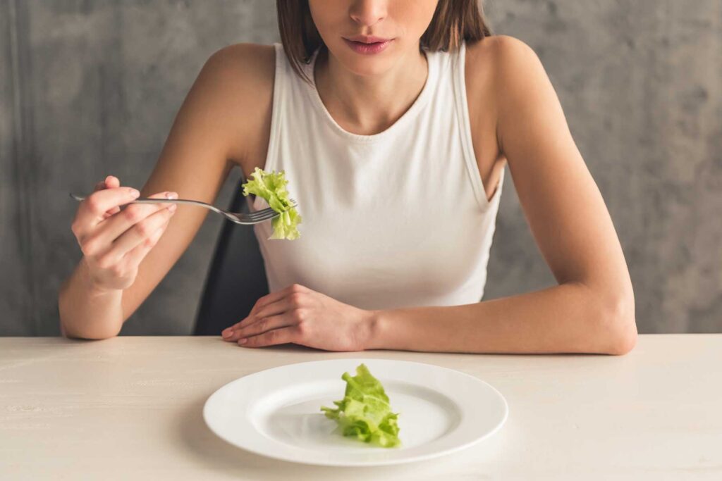 Woman eating tiny bites of salad struggling with the early stages of an eating disorder