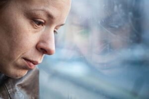 a person looks sadly out a window pondering the role of heredity in depression