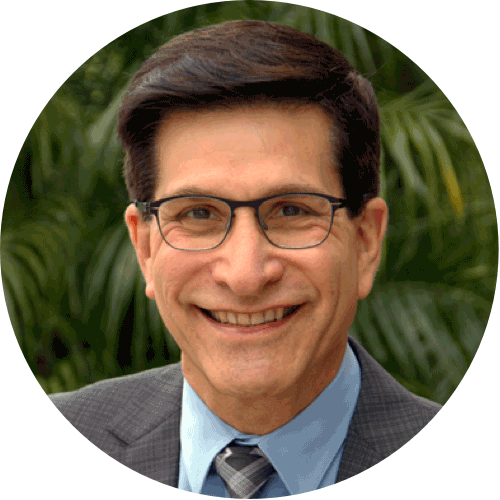A man in a gray suit with a blue shirt and tie smiles comfortingly