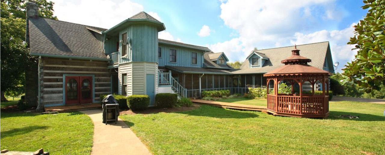 A blue and white two-story house sits on an expansive grass yard with a path leading to a wooden pagoda