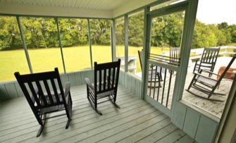 Two wooden rocking chairs sit side by side in an enclosed patio that is painted blue.