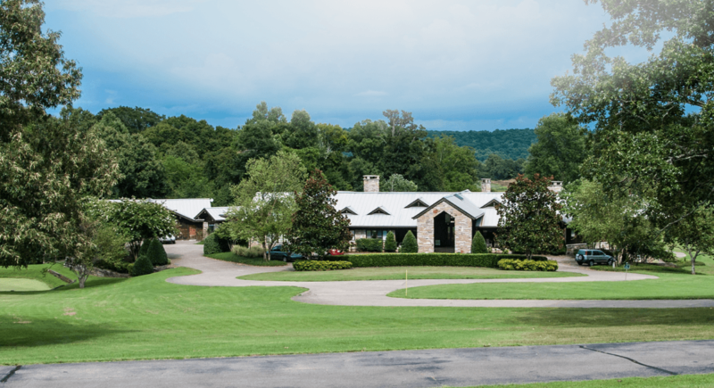 A large house with a long driveway amongst trees, mountains and rolling hills.