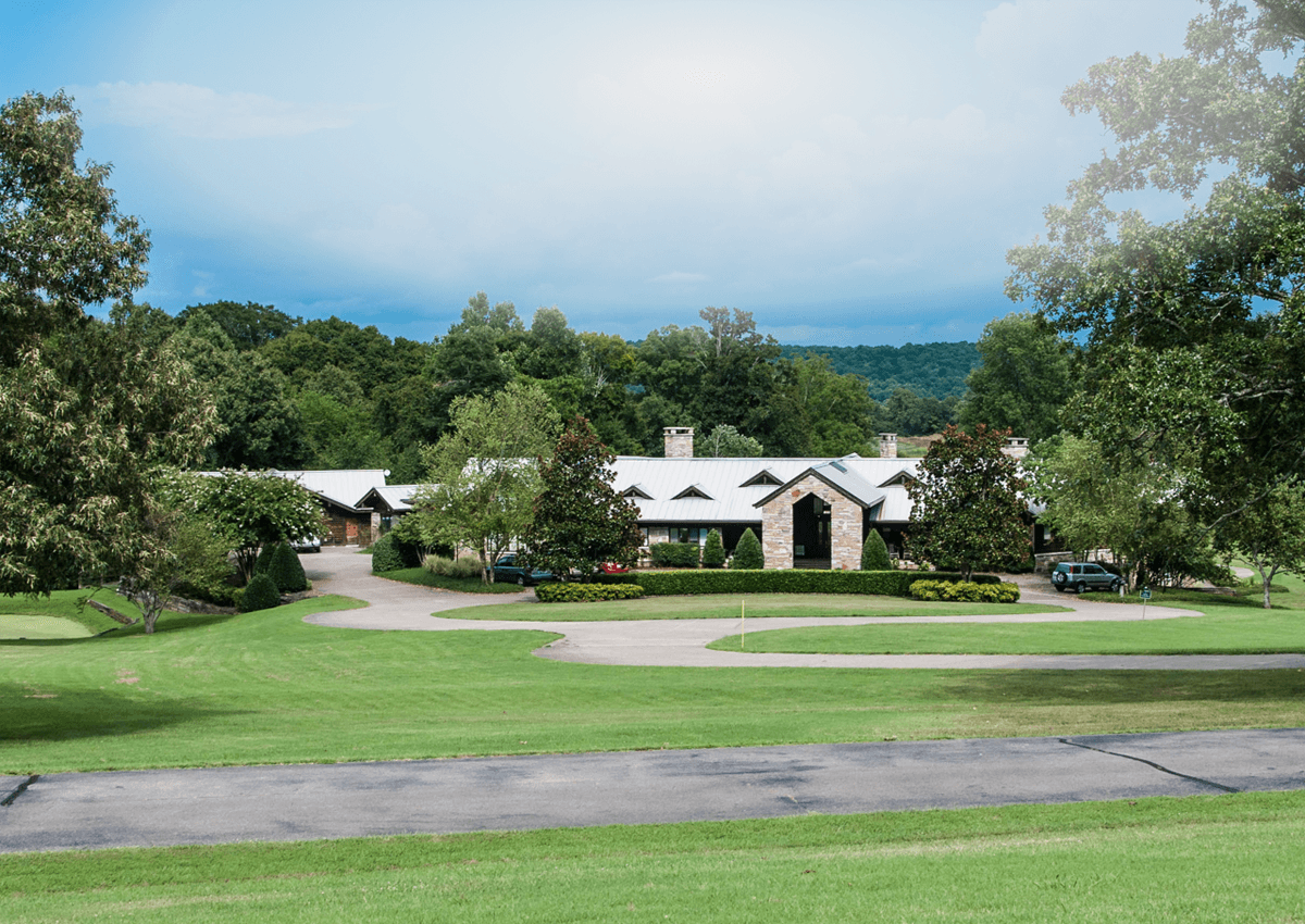 A large house with a long driveway amongst trees, mountains and rolling hills.