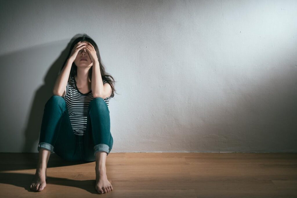 a woman sits on the floor holding her head possibly struggling with common symptoms of bipolar disorder in women