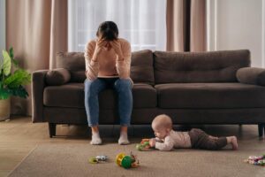 a mother with postpartum depression holds their head while their baby plays