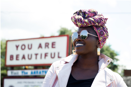 african american woman in colorful head scarf stands in front of billboard that says you are beautiful for national recovery month