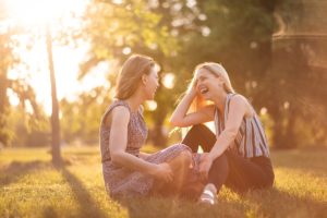 two young women sit in a meadow and talk about their addiction therapy programs