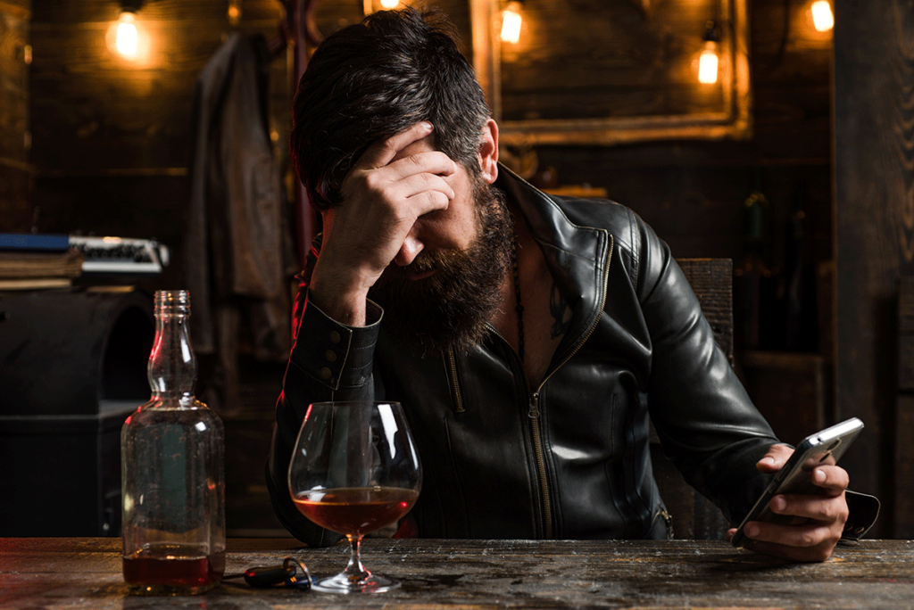 a person holds their head at a bar while dealing with the emotional effects of alcohol