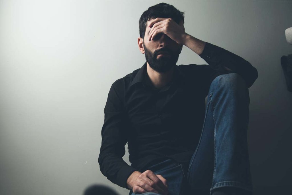 alcohol and depression, man sitting against wall in shadows hand over face