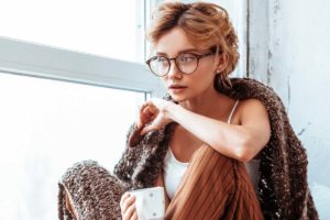 cbt-vs-dbt, woman with glasses sitting next to window with mug and shawl