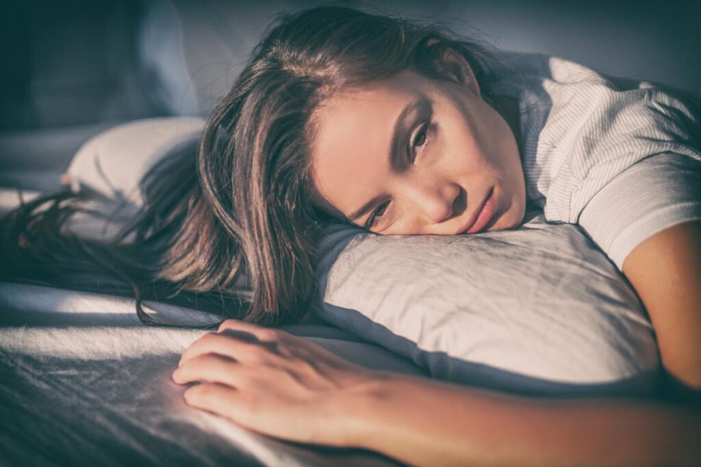 woman laying on bed looking distraught and wondering if CBT for insomnia would help her