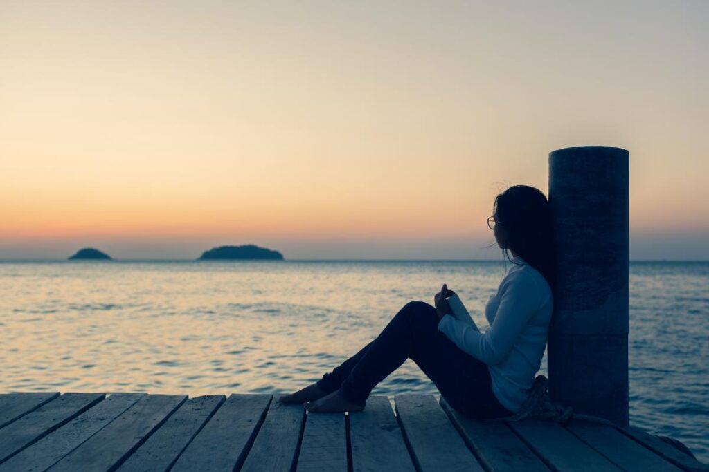 woman sits on pier watching the sunset while thinking about how suicide and meth use can be intertwined