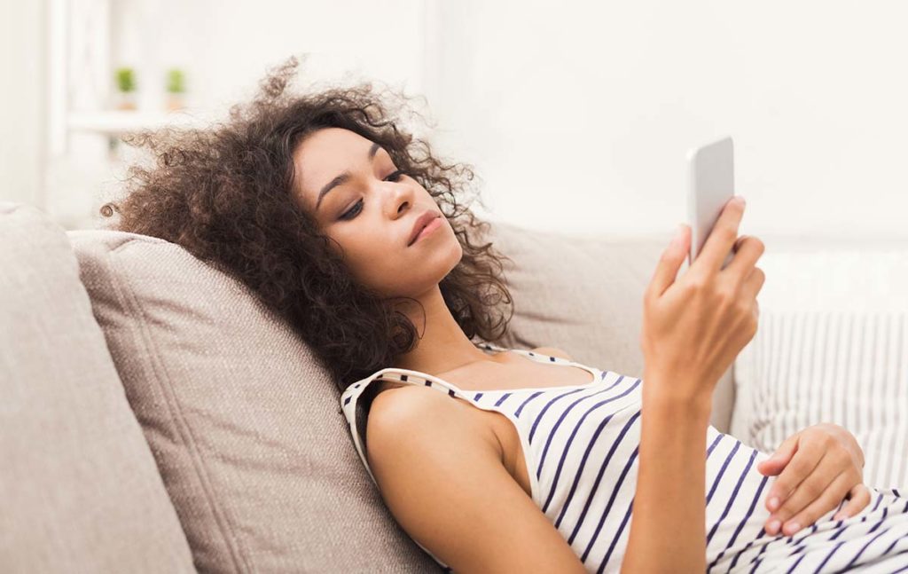 woman on couch searching phone for types of addiction