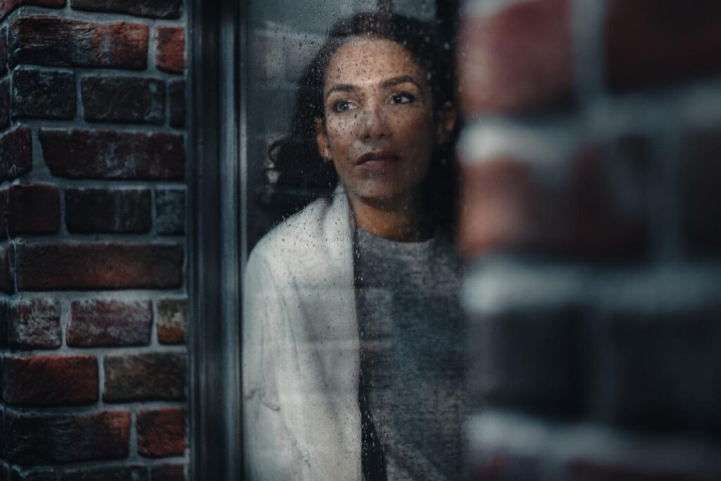 Person pensively looking out window contemplating alcoholism and eating disorders