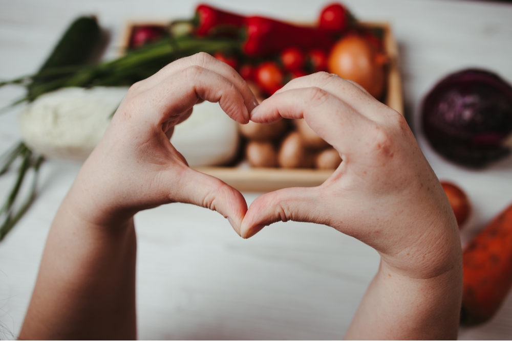 Hands in heart shape with food in background, prompting healthy relationship with food