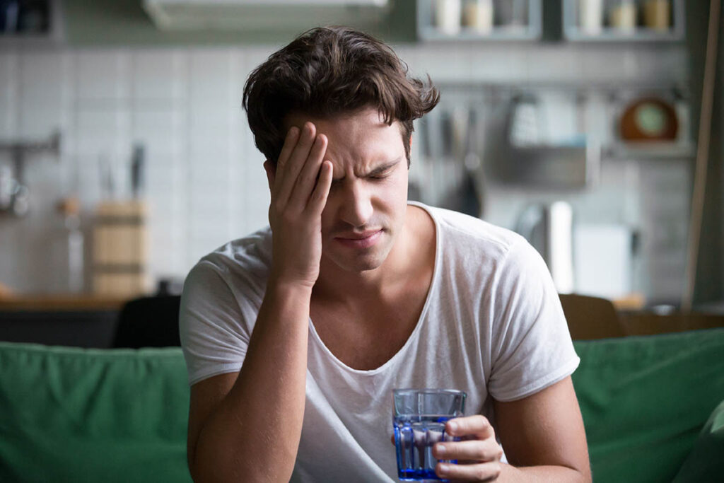 a man holds a glass of water and wonders about the dangers of alcohol withdrawal