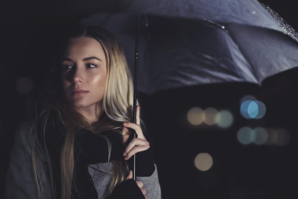 Woman with a faraway stare holding an umbrella while thinking about women and addiction