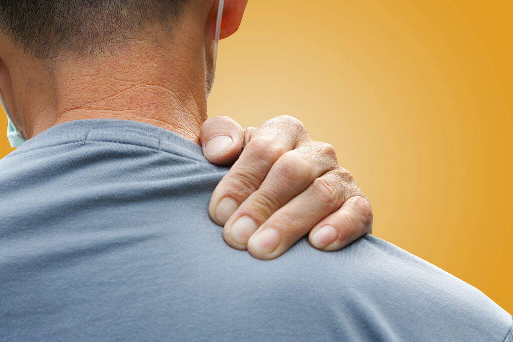 Close-up of a man's back while he massages his own shoulder while experiencing mindfulness therapy and opioid addiction