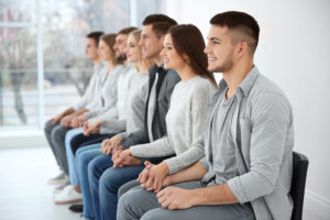 Group of people sitting in a row, wearing various shades of grey, smiling, and holding hands in an alcohol detox program