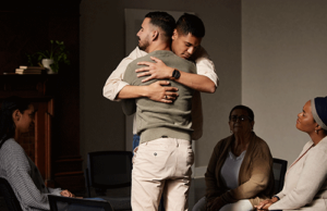 Two people standing and hugging each other in group therapy in aftercare rehab program