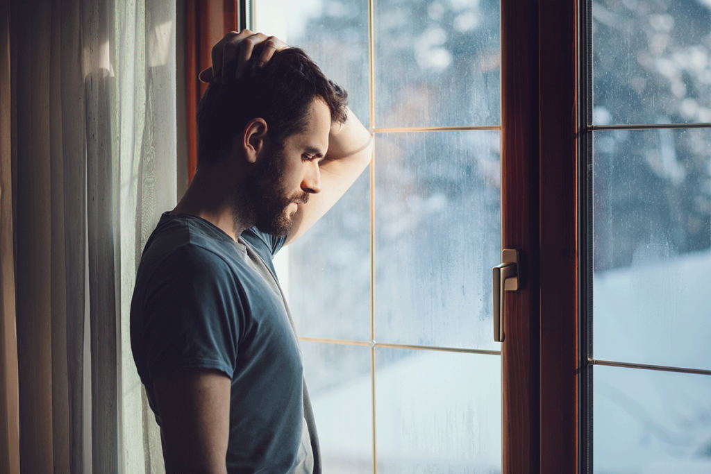 Person looking out window holding onto neck while dealing with chronic pain and recovery