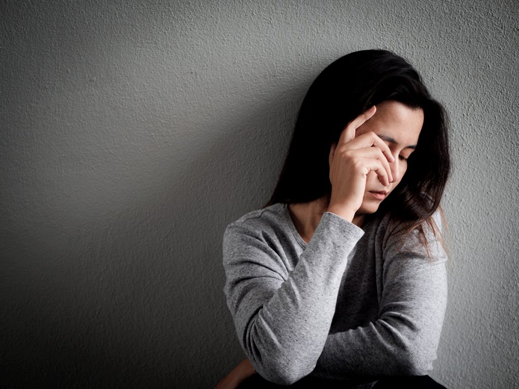 Woman sitting against wall covering face with hand while struggling with signs of Roxicodone abuse