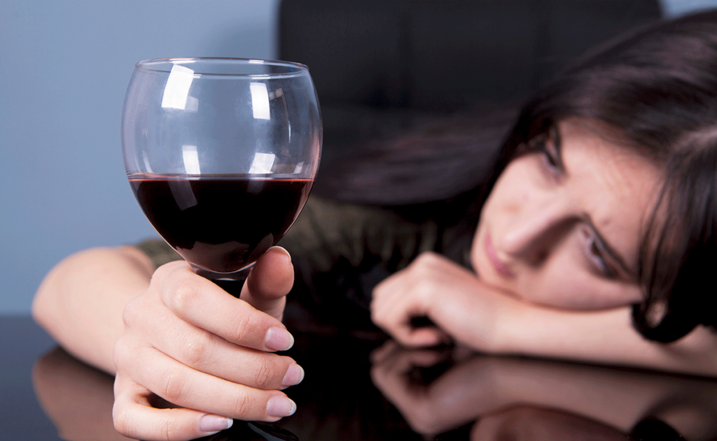 Person holding wine glass with head resting on table struggling with alcohol addiction and depression