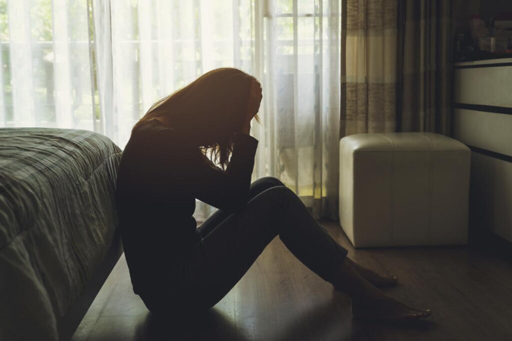 person sitting on floor of dark room with head in hands worried about dangers of using opioids during winter