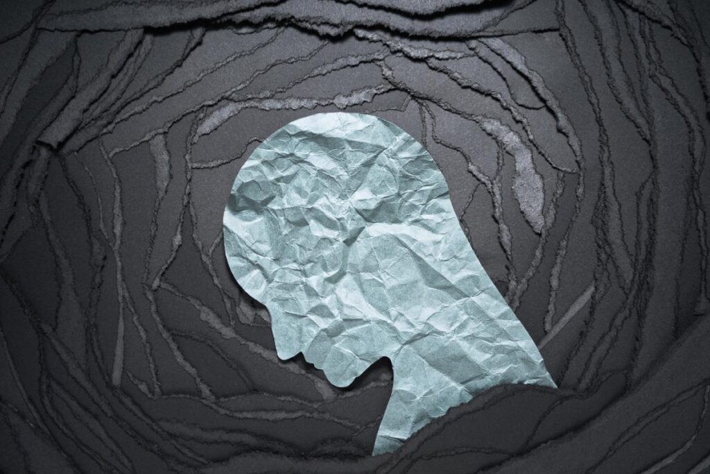 artwork of blue head of depressed person on ripped up black paper to illustrate the question why do drug overdoses increase in winter