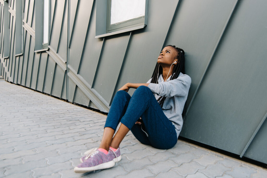 person sitting outside on sidewalk against a wall struggling with symptoms of inhalant abuse