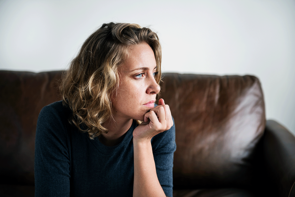 concerned woman sitting on couch wondering what are the symptoms of ptsd in women