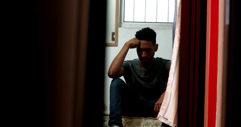 person sitting against door in dark while dealing with heroin dependence