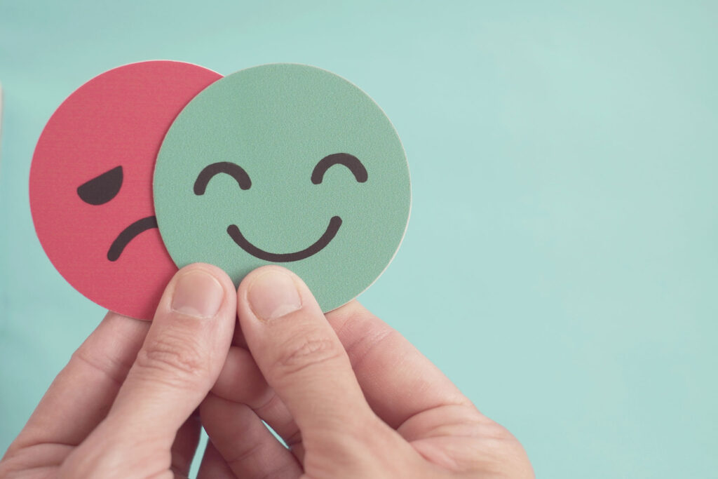 person holding a smiley face and a frowning face while pondering the question is bipolar disorder genetic