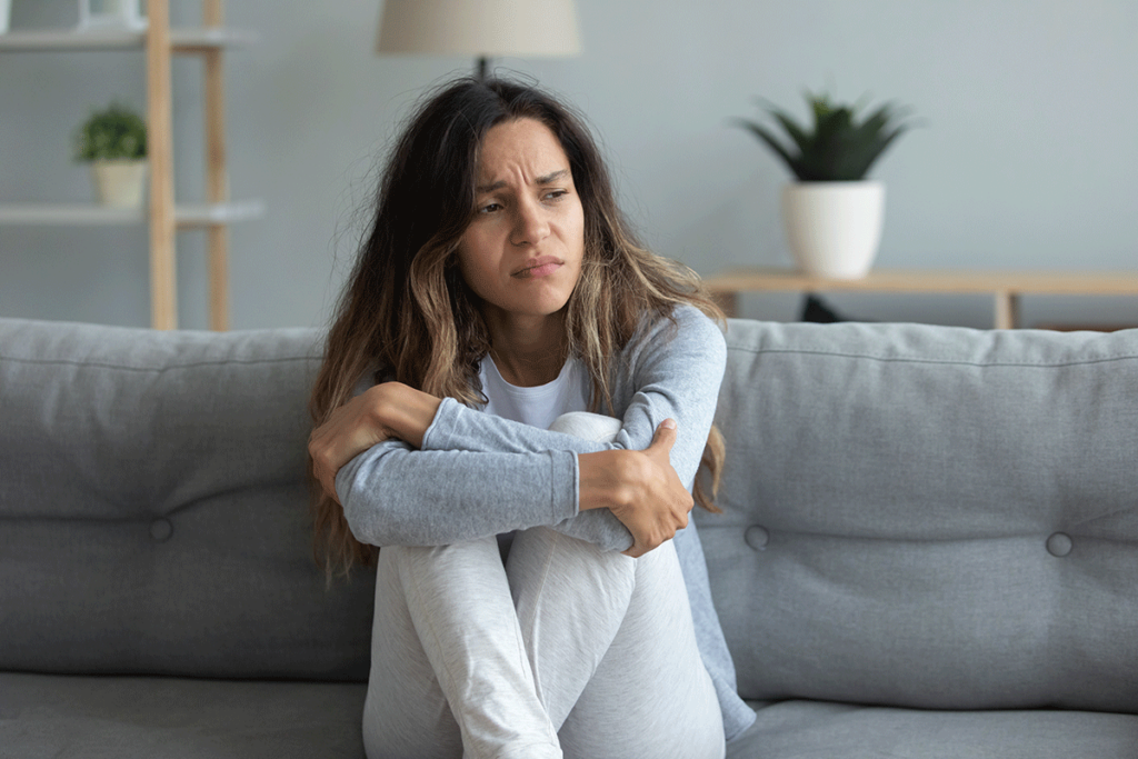 woman on couch with arms around knees struggling with the effects of alcohol on women