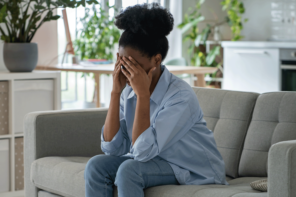 person sitting on couch with hands over face while struggling with anxious avoidant style