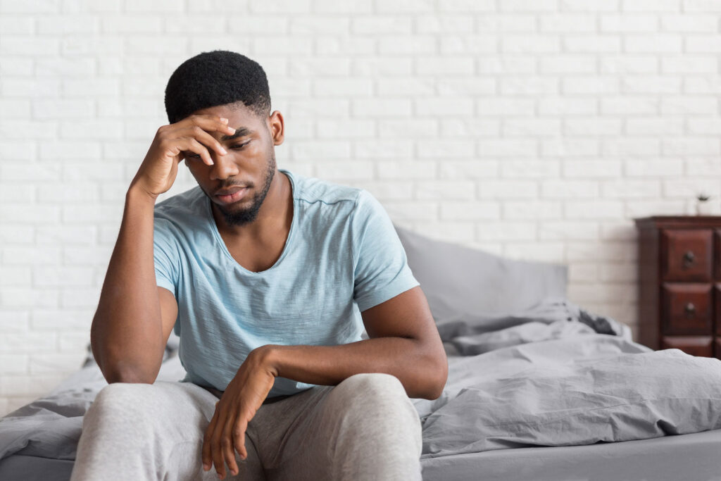 person sitting on edge of bed touching forehead while experiencing post acute withdrawal syndrome
