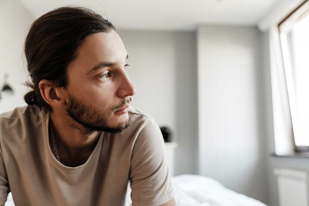 person sitting on edge of bed looking out window while struggling with adderall abuse