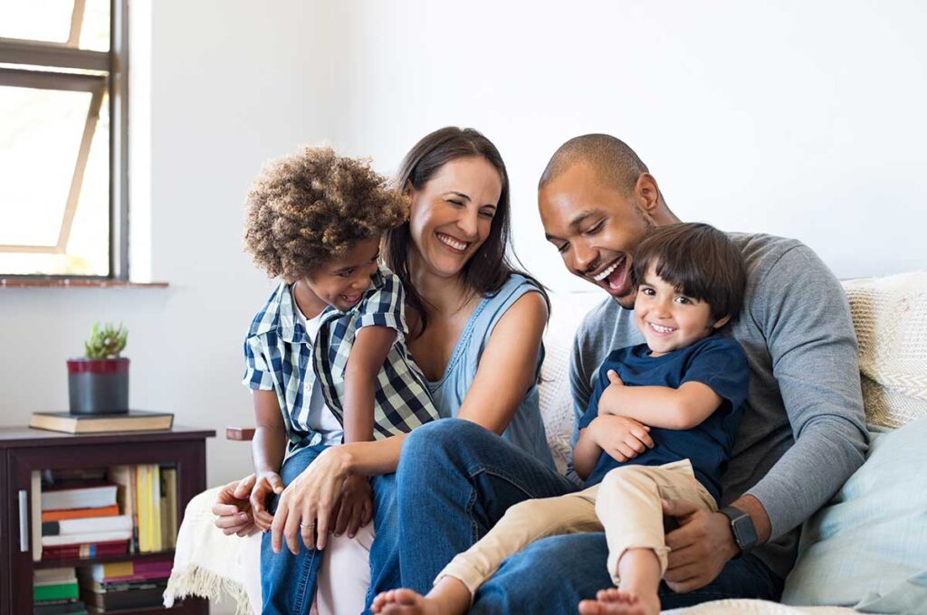 family of four smiling while spending time on couch after learning what is family counseling